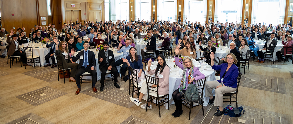 Scholarship donors and medical students smiling while sitting at tables and waving at the camera